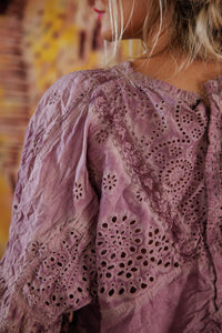 Close-up of a person wearing a purple embroidered blouse with a blurred background