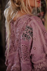 Purple lace garment with text on the back, worn by a person with long blonde hair.